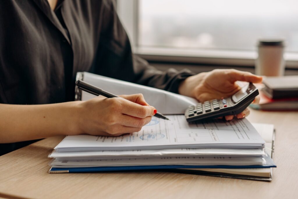 Pessoa com calculadora na mão e fazendo anotações para conseguir guardar dinheiro